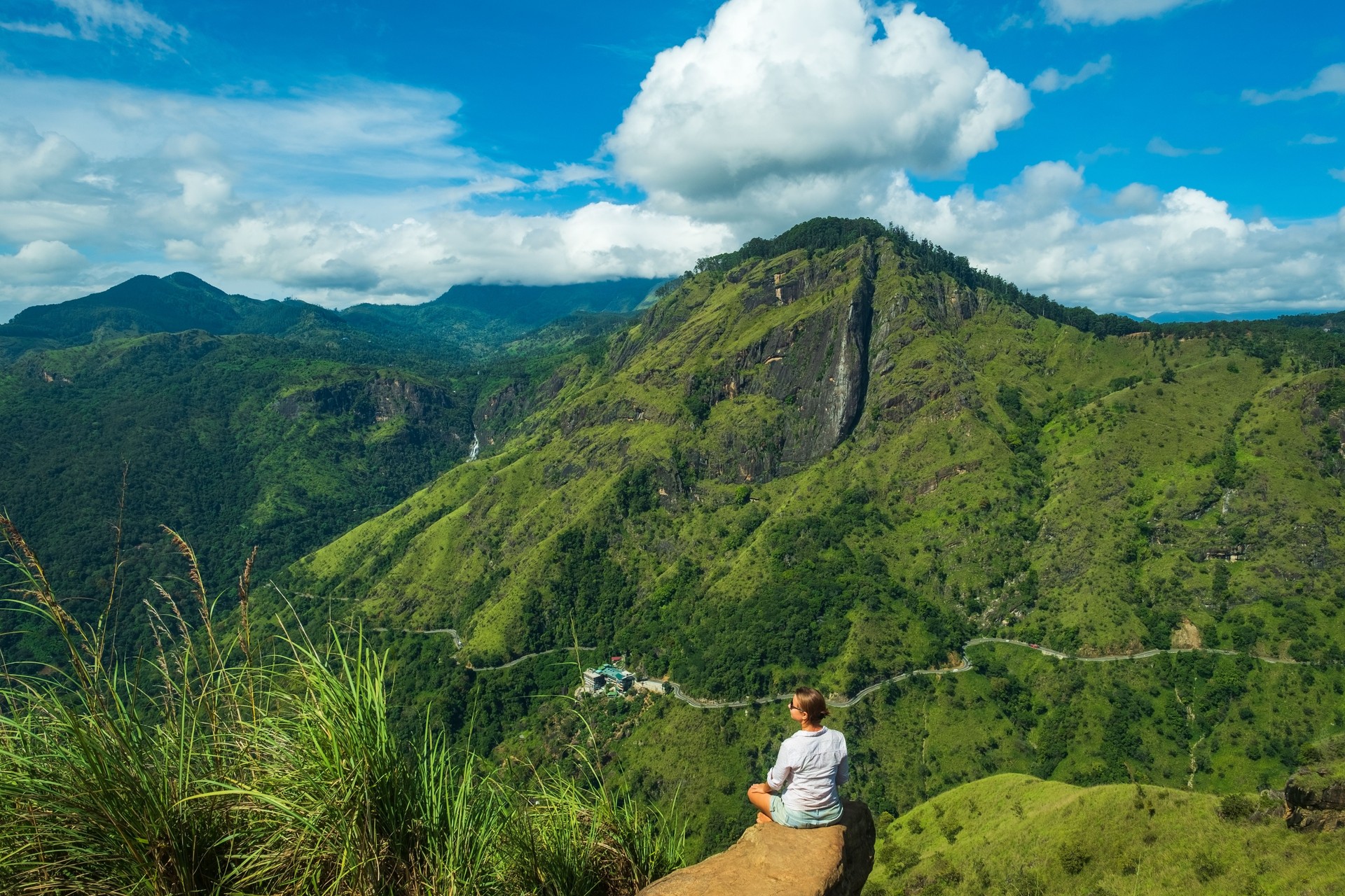 woman sitting on stone on Mini Adams peak looking on green mountains of Sri Lanka